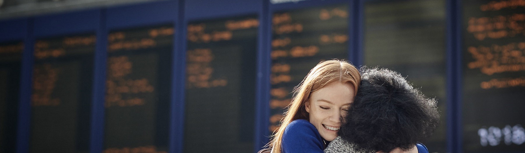 Ladies hugging with a train departure board behind them 