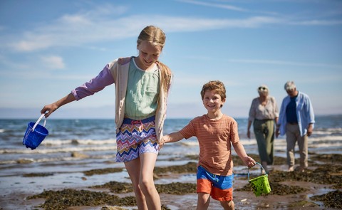 Young girl and boy running on beach with grandparents walking behind them